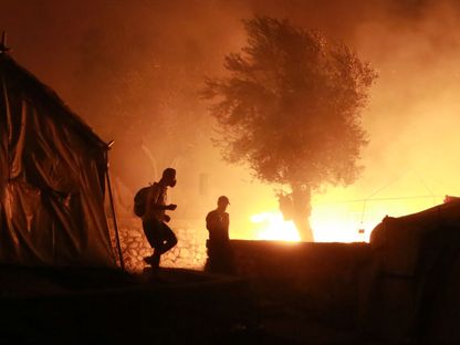 مهاجرون يسيرون داخل مخيم موريا في جزيرة ليسبوس اليونانية خلال حريق كبير - AFP