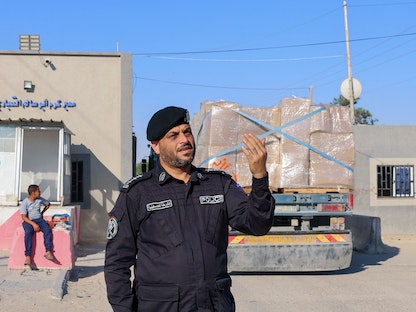 ضابط شرطة فلسطيني أمام شاحنات محملة بأقمشة من المقرر تصديرها عبر معبر كرم أبو سالم جنوب قطاع غزة- 21 يونيو 2021 - AFP
