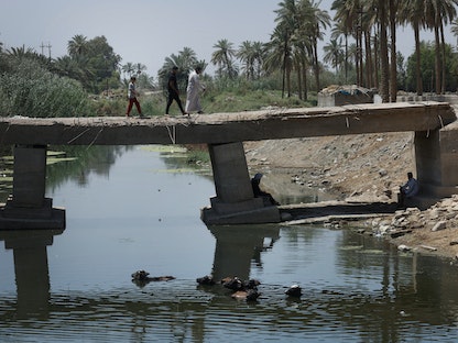 أشخاص يعبرون جسراً فوق نهر الشلال في منطقة المشخاب بضواحي النجف في العراق. 23 يونيو 2023 - REUTERS