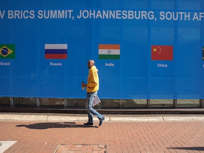 رجل يمر بجانب لافتة خارج مقر قمة "بريكس 2023" بمدينة ساندتون شمال جوهانسبرج في جنوب إفريقيا. 20 أغسطس 2023 - AFP