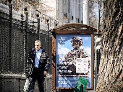 رجل أمام لوحة إعلانية تظهر جندياً روسياً بعبارة "مهنتنا الدفاع عن الوطن الأم" في موسكو -12 أبريل 2023 - AFP