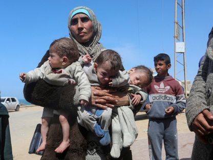 امرأة فلسطينية تحمل أطفالها الثلاثة بعد اضطرارها إلى مغادرة مستشفى الشفاء إثر غارة إسرائيلية وسط قطاع غزة. 21 مارس 2024 - Reuters