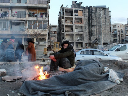 رجل يجلس في أحد شوارع مدينة حلب السورية بجوار آخر نائم. 8 فبراير 2023 - REUTERS