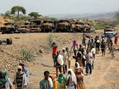 قرويون في إحدى القرى بإقليم تيجراي شمال إثيوبيا يسيرون بجانب آليات عسكرية محترقة - 10 يوليو 2021 - REUTERS