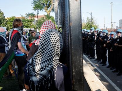 أفراد من شرطة مكافحة الشغب يقفون أمام المتظاهرين بالقرب من مقر انعقاد المؤتمر الوطني الديمقراطي في شيكاجو. 19 أغسطس 2024 - REUTERS