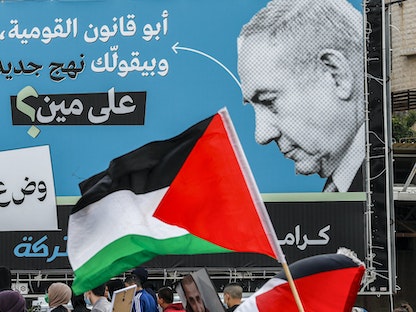 علم فلسطيني أمام لوحة دعائية انتخابية لحزب "القائمة العربية الموحدة" في إسرائيل تهاجم رئيس الوزراء بنيامين نتنياهو - 12 مارس 2021 - AFP
