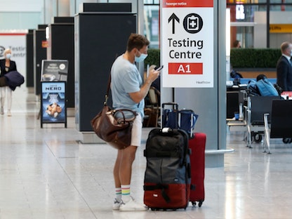 مسافر يقف بجوار لافتة مركز اختبار كورونا في مطار هيثرو بالعاصمة البريطانية لندن - 2 أغسطس 2021  - REUTERS