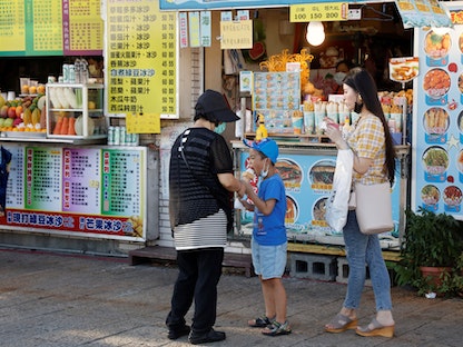 طفل يأكل المثلجات أمام كشك للطعام بمدينة تايبيه الجديدة شمال تايوان. 7 أغسطس 2022 - REUTERS