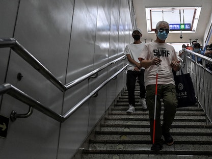 تشانغ شين شنغ، يسير على الدرج بعصاه في محطة مترو أنفاق في بكين. وقد حضر العشرات من رواد السينما المكفوفين عروض سينما بمساعدة متطوعين، 7 أغسطس 2021 - AFP