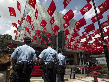 شرطيون تحت أعلام للصين وهونغ كونغ في المدينة، 1 يوليو 2021 - Bloomberg