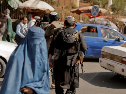 امرأة ترتدي البرقع وتسير في أحد شوارع كابول بينما يظهر عناصر من قوات طالبان في دورية، أفغانستان. 3 أكتوبر 2021. - REUTERS