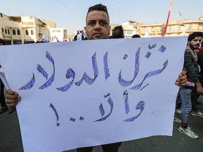 عراقي يحمل لافتة تطالب بخفض سعر صرف الدولار خلال احتجاجات في العاصمة العراقية بغداد. 25 يناير 2023 - AFP