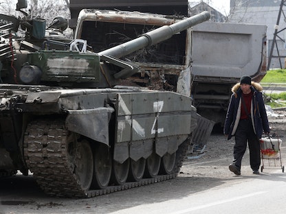أوكراني يسير بجانب دبابة تابعة للقوات الموالية لروسيا في مدينة ماريوبل. 19 أبريل 2022 - REUTERS