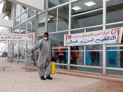 رجل يرتدي بدلة واقية يرش مطهراً أمام مركز التطعيم ضد فيروس كورونا في تونس العاصمة. 13 مارس 2021 - REUTERS
