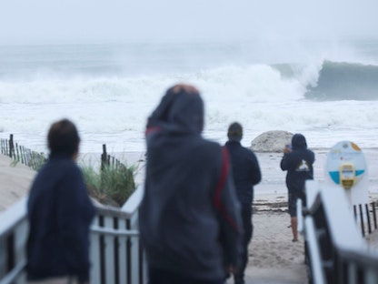  أشخاص يشاهدون الأمواج في شاطئ بونكووج حيث يمر إعصار هنري الذي انخفض الآن إلى عاصفة استوائية بالقرب من الساحل في لونج آيلاند، نيويورك، الولايات المتحدة، 22 أغسطس 2021 - REUTERS