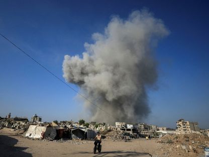 رجل فلسطيني يركب دراجة هوائية بينما يتصاعد الدخان بعد غارة إسرائيلية في مدينة غزة. 24 أغسطس 2025 - reuters