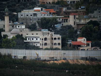 قرية كفركلا الحدودية اللبنانية تظهر خلف الجدار بينما يعمل أفراد الجيش الإسرائيلي والآليات الثقيلة على الجانب الإسرائيلي من الحدود - REUTERS