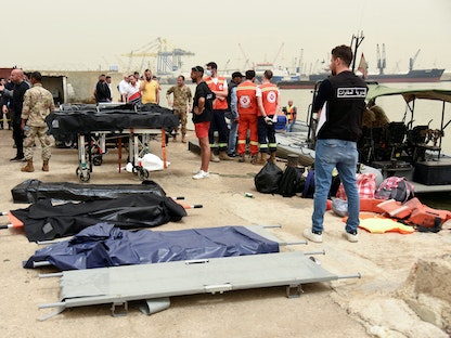 أشخاص يقفون بالقرب من نقالات جاهزة لاستقبال الجثث بعد انقلاب قارب قبالة ساحل طرابلس - 24 أبريل 2022 - REUTERS