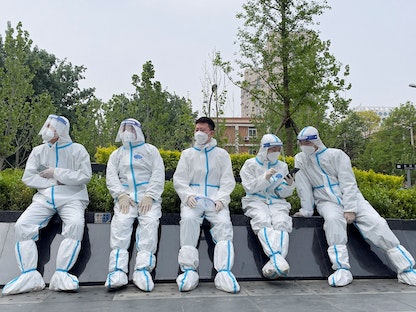 عمال في المجال الطبي يرتدون بدلات واقية يستريحون قرب موقع لاختبار كورونا في العاصمة الصينية بكين. 29 أبريل 2022 - REUTERS