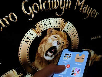 شعار أمازون على هاتف ذكي أمام أسد استدوديوهات MGM الشهير، على شاشة كمبيوتر في لوس أنجلوس - AFP