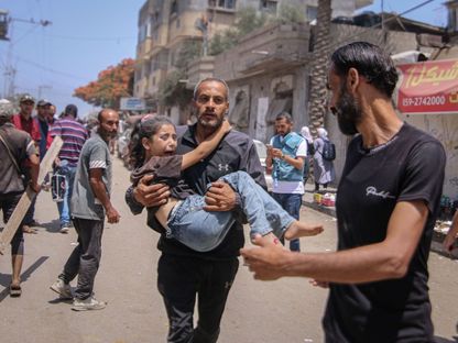 رجل يحمل طفلة مصابة بعد الهجوم الإسرائيلي على مخيم النصيرات في غزة. 08 يونيو 2024 - Bloomberg