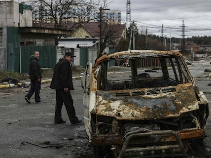 سيارة مدمرة وخلفها جثث ملقاة على طريق عام في منطقة بوتشا في ضواحي العاصمة الأوكرانية كييف - 03 أبريل 2022 - AFP