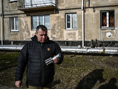 أحد الأشخاص يحمل بقايا قذيفة هاون انفجرت أمام مبنى مدينة لوهانسك في شرق أوكرانيا - 22 فبراير 2022 - AFP