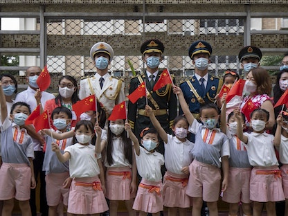 تلاميذ يحملون أعلاماً صينية مع أعضاء في حرس الشرف بالجيش الصيني خلال إحياء ذكرى عودة هونج كونج إلى الحكم الصيني - 1 يوليو 2021 - Bloomberg