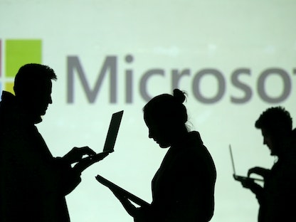 صورة توضيحية لأشخاص يحملون حواسيب أمام شعار "مايكروسوفت" - REUTERS