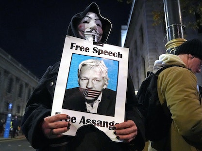 متظاهر مناهض للرأسمالية يحمل صورة لمؤسس ويكيليكس جوليان أسانج في تجمع بميدان ترافالغار في لندن -5 نوفمبر 2020. - AFP