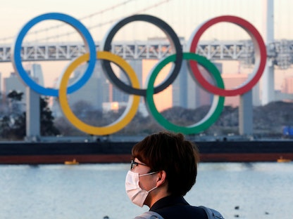 رجل يرتدي قناعا واقيا وسط تفشي فيروس كورونا أمام الحلقات الأولمبية العملاقة في طوكيو باليابان . - REUTERS