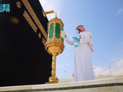 مسؤول من مكتب الرئيس العام لشؤون الحرمين الشريفين ينظف ويعطر محيط الكعبة في المسجد الحرام، مدينة مكة المكرمة، 14 أبريل 2021 - REUTERS