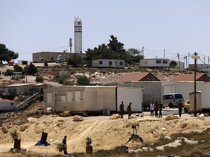 مستوطنون وجنود إسرائيليون يقفون قرب مدخل قرية جالود بالضفة الغربية. 31 مايو 2023 - AFP