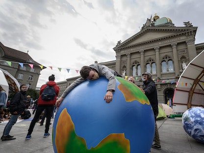 ناشط يحتضن مجسماً للكرة الأرضية خلال مظاهرات "نهضوا للتغيير" في برن، سويسرا، 21 سبتمبر 2020 - AFP