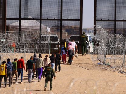 أفراد من حرس الحدود الأميركي يرافقون مهاجرين عبروا الحدود بين الولايات المتحدة والمكسيك من خلال بوابة في الجدار الحدودي عند مدينة سيوداد خواريز في المكسيك. 5 أكتوبر 2023 - Reuters