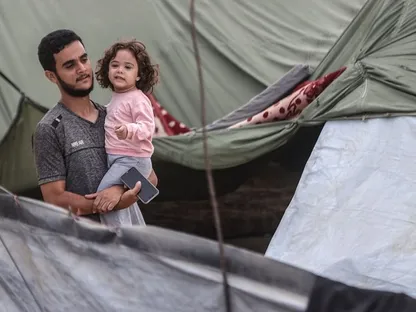 أب فلسطيني يحمل ابنته بين خيام النازحين في خان يونس جنوبي قطاع غزة في أعقاب إعلان اتفاق وقف إطلاق النار. 9 أكتوبر 2025 - Getty Images