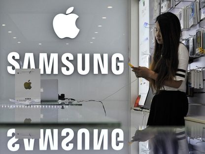 مسؤولة مبيعات تستخدم هاتفها المحمول بجوار شعارات شركة Apple و Samsung في متجر بمقاطعة أنهوي في الصين. 10 سبتمبر 2014 - Reuters