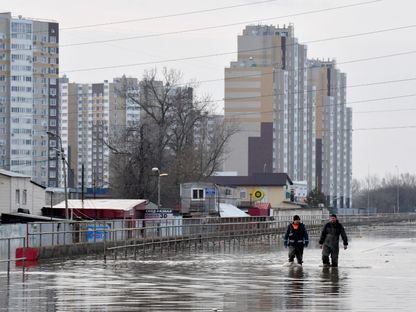 عمال الإنقاذ يسيرون في شارع غمرته مياه الفياضانات في مدينة أورينبورج الروسية. 13 أبريل 2024 - AFP