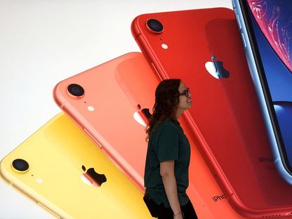 موظفة بأحد متاجر أبل في واشنطن تمر أمام إعلان لهواتف آيفون. 9 مايو 2019 - REUTERS