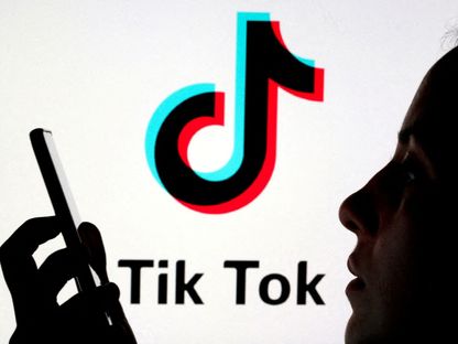 شخص يحمل هاتفاً ذكياً أمام رسم توضيحي لشعار "تيك توك". 7 نوفمبر 2019 - REUTERS