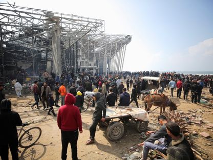 فلسطينيون في قطاع غزة يتجمعون بانتظار أكياس الطحين المحملة على شاحنات المساعدات بالقرب من نقطة تفتيش إسرائيلية. 19 فبراير 2024 - Reuters