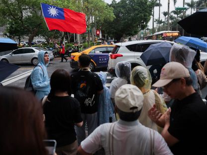 رجل ترافقه الشرطة يحمل العلم التايواني وعلى الجانب الآخر حشد من الأشخاص في العاصمة التايوانية تايبيه. 24 مايو 2024 - reuters
