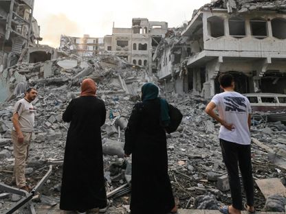 فلسطينيون يقفون أمام ركام أحد المنازل في حي الرمال بغزة في أعقاب ضربة جوية إسرائيلية. 10 أكتوبر 2023 - AFP