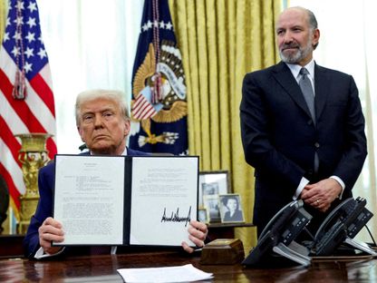 الرئيس الأميركي دونالد ترمب يحمل أمراً تنفيذياً بشأن زيادة التعريفات الجمركية وإلى جواره وزير التجارة الأميركي هوارد لوتنيك في المكتب البيضاوي. 13 فبراير 2025 - REUTERS