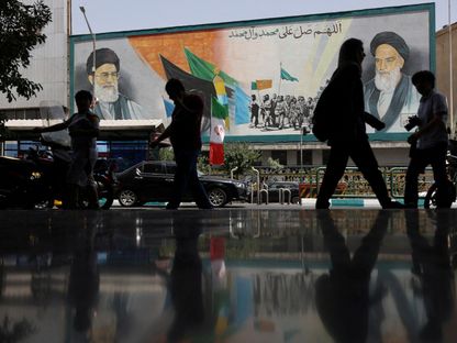 إيرانيون يسيرون بجوار لوحة جدارية عليها صورة المرشد الإيراني علي خامنئي في أحد شوارع العاصمة طهران في الساعات الأولى من دخول اتفاق وقف إطلاق النار حيز التنفيذ، طهران، إيران. 24 يونيو 2025 - REUTERS