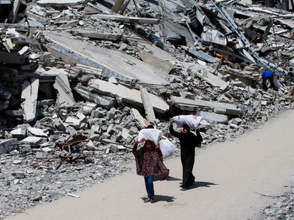 امرأة فلسطينية وفتاة تحملان أكياس وتسيران على أنقاض منازل في مدينة غزة. 20 مايو 2025 - رويترز