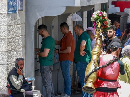 فلسطينيون يصطفون لسحب الأموال من جهاز صراف آلي في السوق الرئيسي بمدينة رام الله في الضفة الغربية التي تحتلها إسرائيل. 9 يونيو 2024 - AFP
