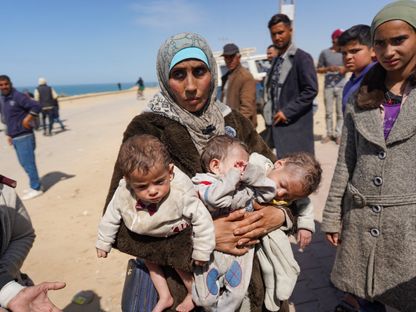 امرأة تحمل ثلاثة أطفال عند وصولها إلى الجزء الأوسط من قطاع غزة بعد فرارها من مجمع مستشفى الشفاء في مدينة غزة. 21 مارس 2024 - AFP