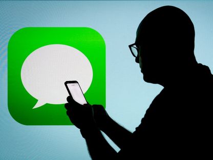 شخص يحمل هاتفاً وخلفه شعار تطبيق iMessage للتراسل في العاصمة البولندية وارسو. 21 يوليو 2023 - AFP