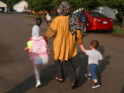لاجئة أفغانية تمشي مع أطفالها نحو حافلة المدرسة في بولينج جرين بولاية كنتاكي الأميركية. 30 أبريل 2025. - REUTERS
